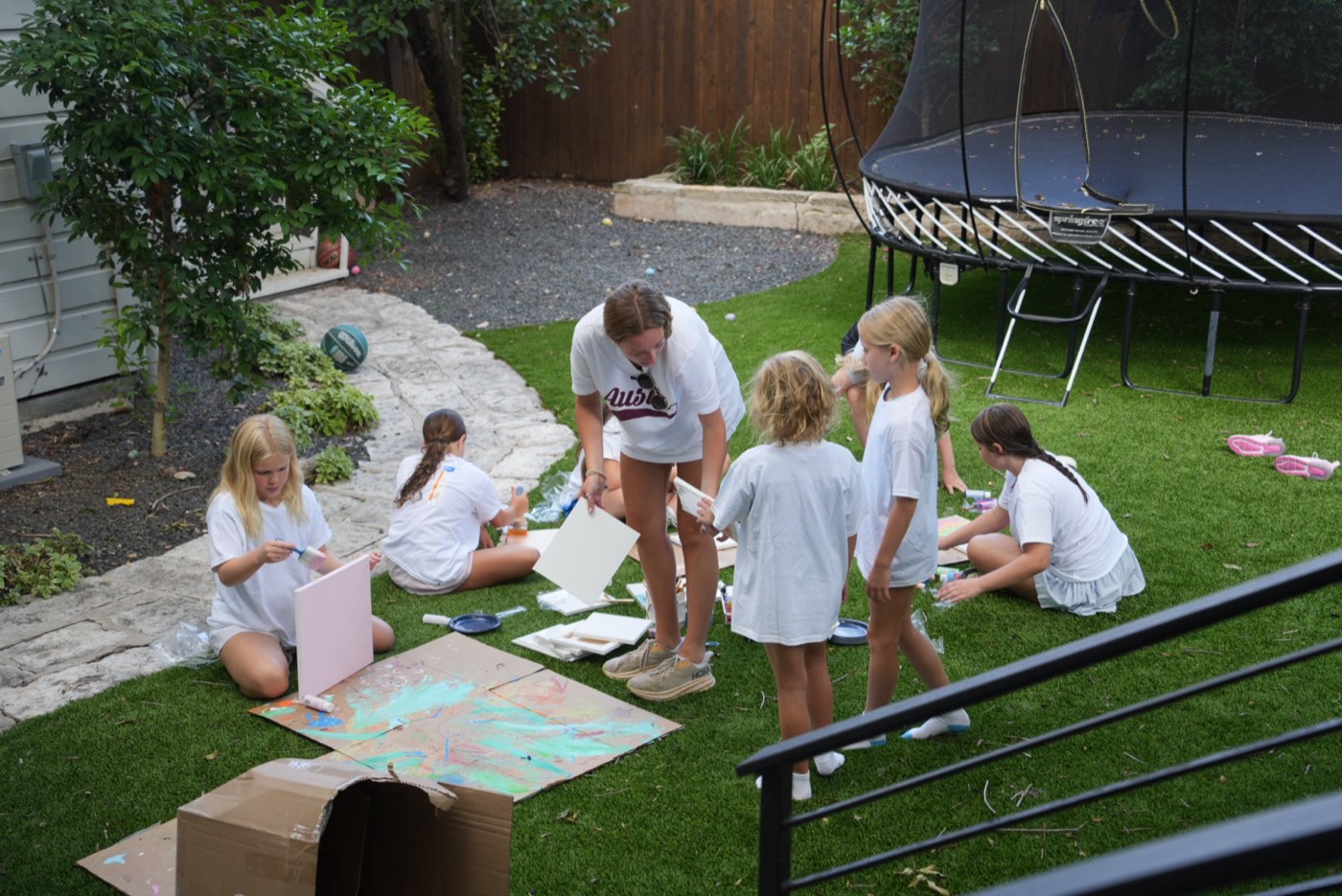 A counselor bending down to help a group of campers with their canvases.