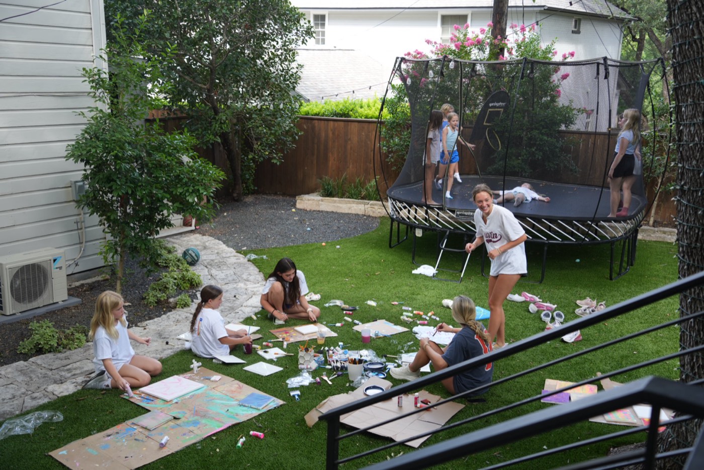 A camp counselor laughing while campers paint on the lawn behind her.