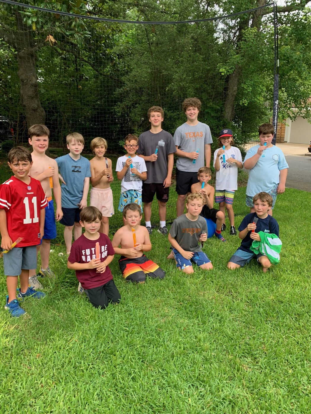 About fourteen boy campers and two teenage counselors posing on the lawn with popsicles.