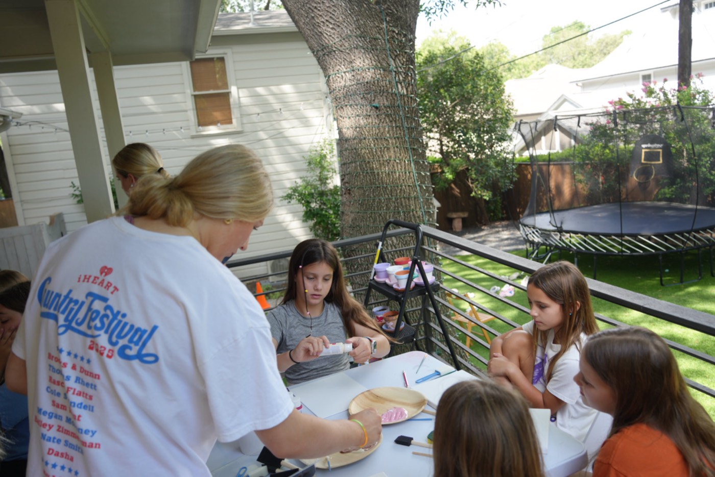 A counselor helping campers decorate pots at an outdoor craft table.