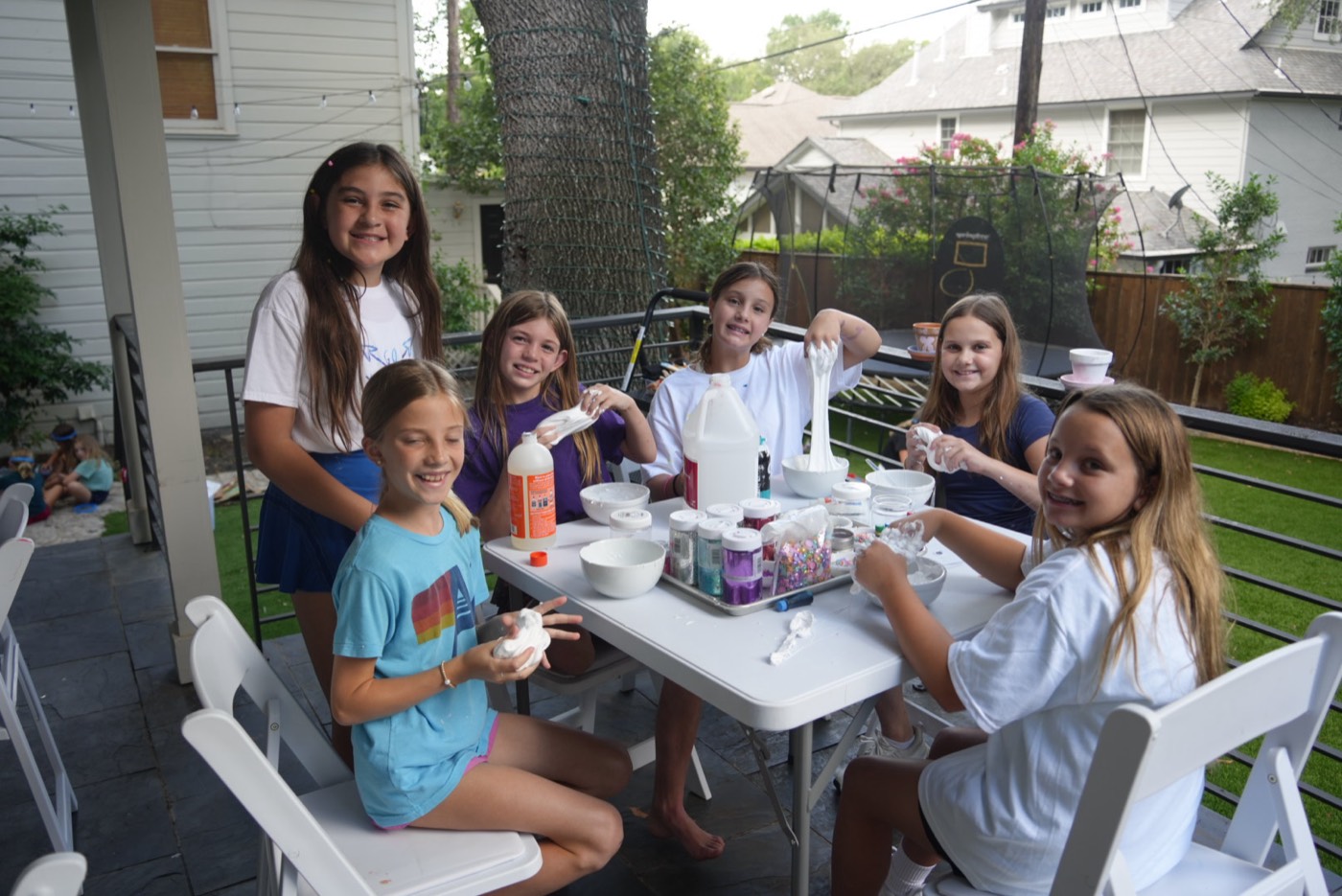 Six campers around a table stretching handfuls of white slime and smiling.