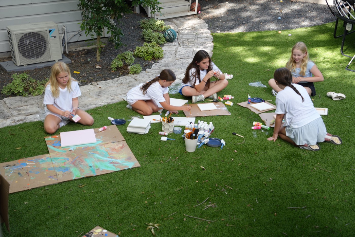 Campers painting canvases on the lawn.